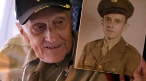 A World War II veteran brings along a photo of himself as a soldier in his youth. His volunteer travel companion, or “guardian,” holds the picture up for him on their flight to Washington, DC. / Photo courtesy of Freethink Media